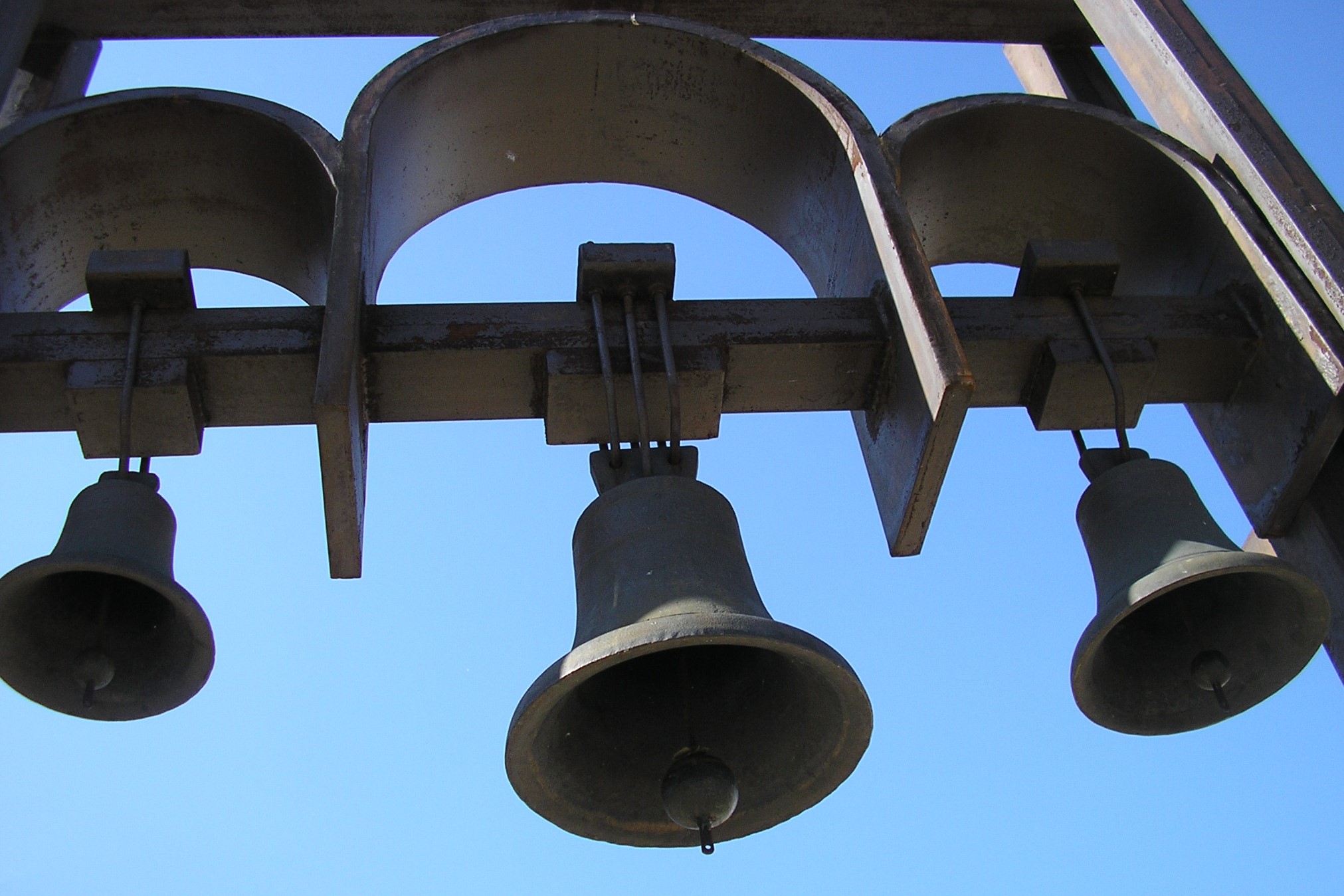 Three church bells ringing against a blue sky.