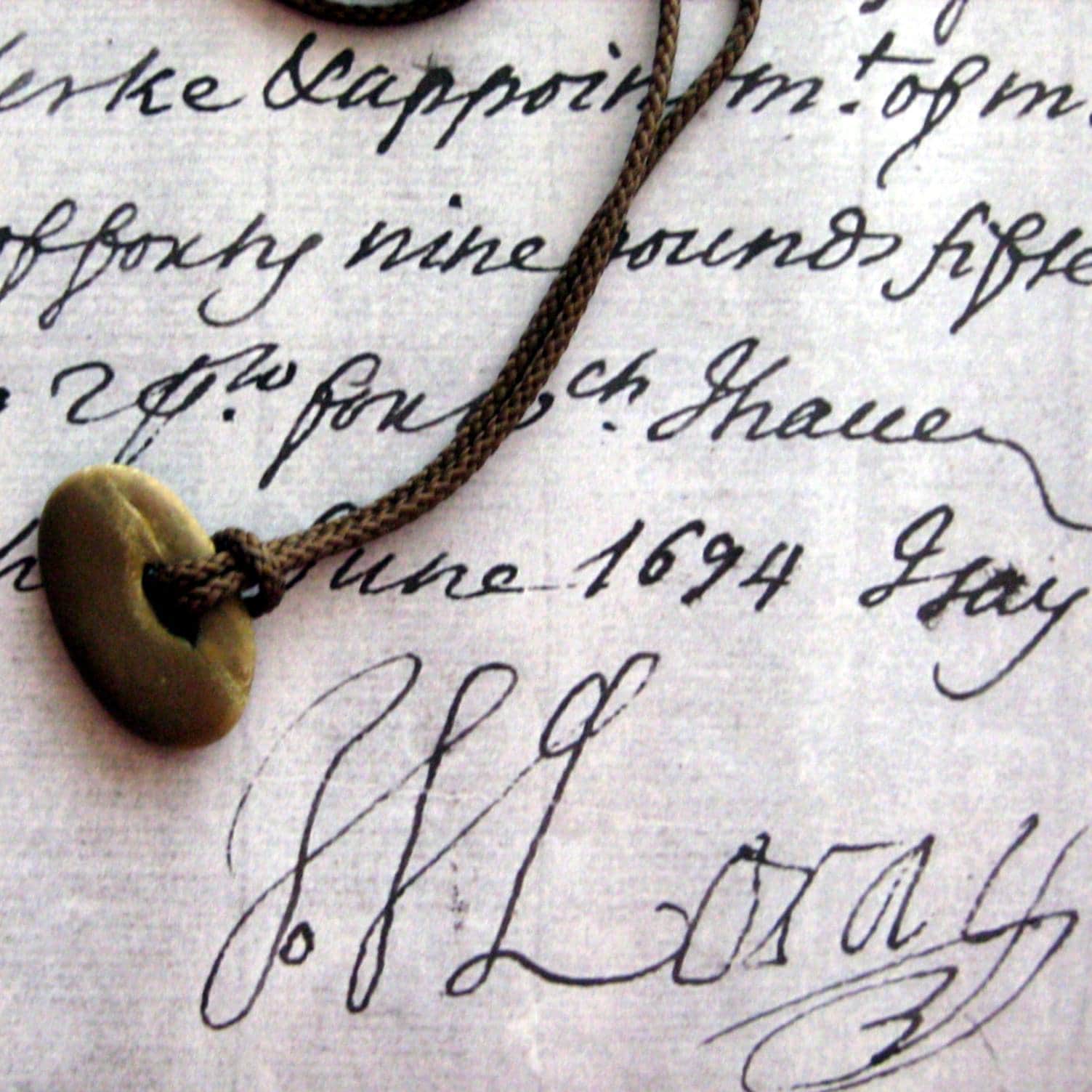 A small stone with a hole in it strung on a cord lies on top of a handwritten letter dated 1694 and signed "J Moray" - the signature of John Moray.