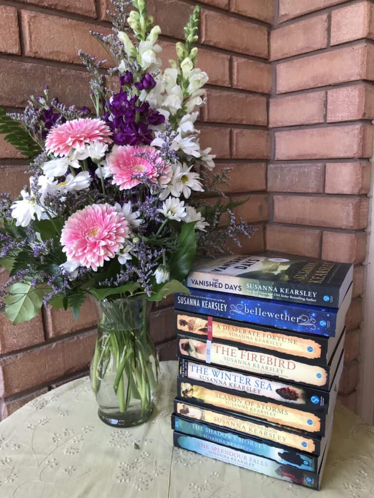 An elaborate bouquet of flowers in a glass vase sits on a table beside a stack of Susanna Kearsley's novels. The flowers were sent to her by Sourcebooks in 2021 to celebrate the one millionth copy of their editions of her books sold in the USA.